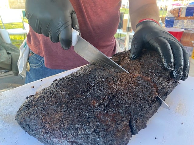 A whole smoked brisket being carved with a slicing knife.