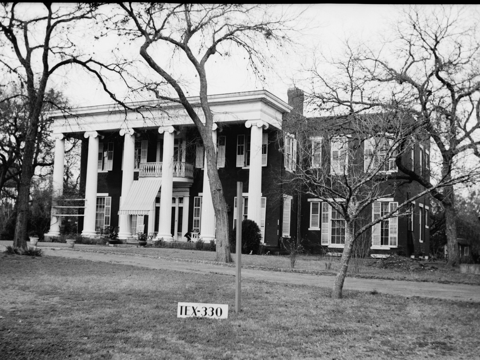 Woodlawn, the Greek Revival mansion of Governor Elisha M. Pease in Austin — a two-story brick house behind a six-columned Ionic portico, photographed in winter for the Historic American Buildings Survey, with a small TEX-330 survey placard standing on the lawn.